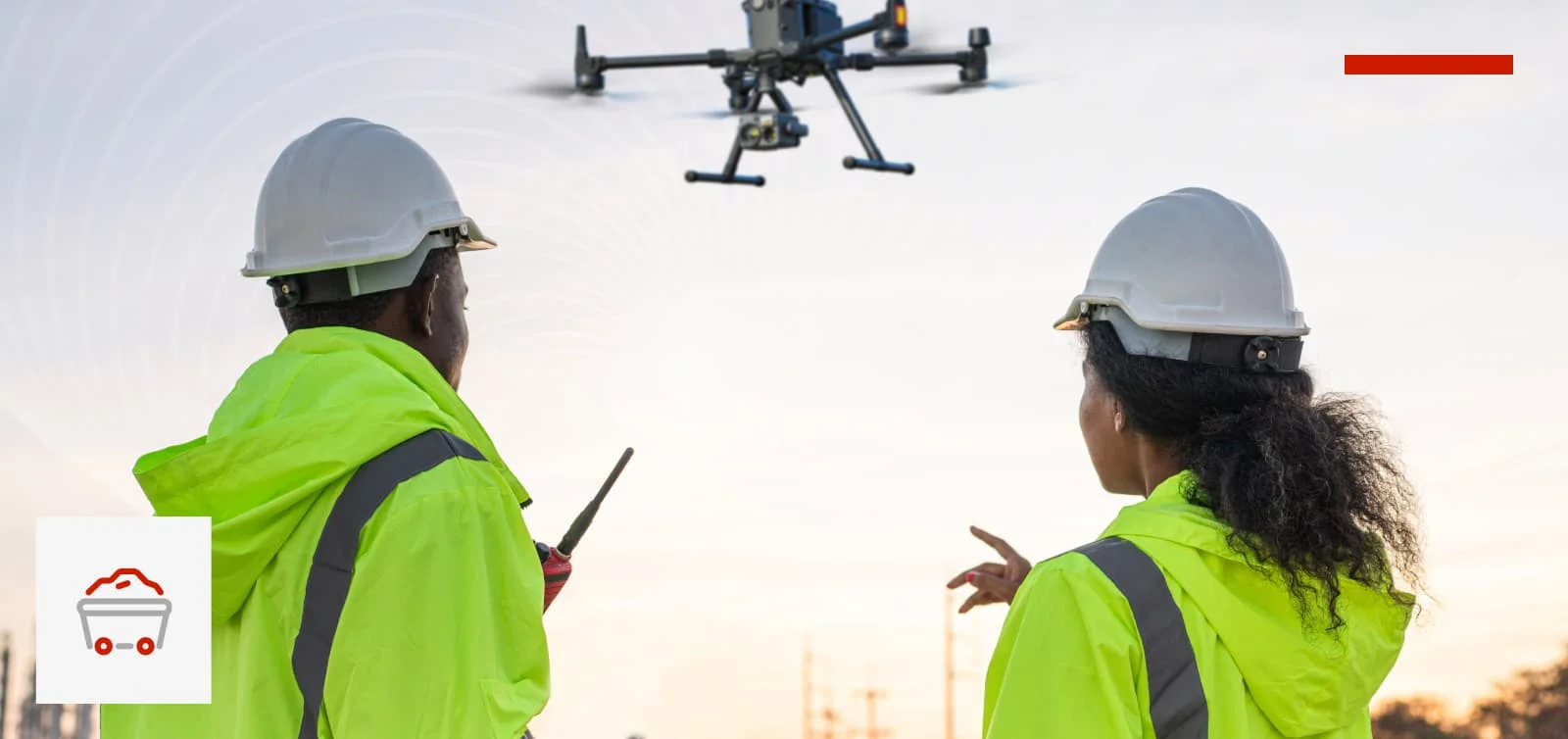 Two people in high vis jackets observing an enterprise-grade DJI M30 drone, with the person on the right pointing at the drone, with a background of a remote site facility.